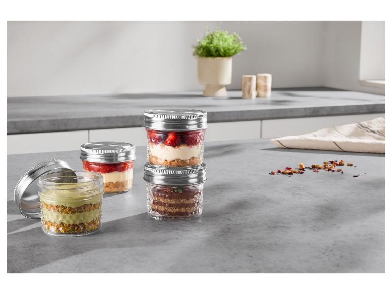 Desserts in Gläsern auf einer Küchenarbeitsplatte, darunter Erdbeer-, Pistazien- und Schokoladenvarianten.