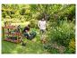 Paar im Garten mit Rasenmäher, Trimmer und Gartentisch mit Werkzeugen.
