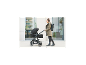 Frau schiebt einen schwarzen Kinderwagen mit Babywanne, gekleidet in grüne Jacke und schwarze Hose.