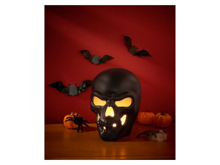 Schwarzer beleuchteter Totenkopf mit dekorativen Fledermäusen, Kürbissen und Spinnen.