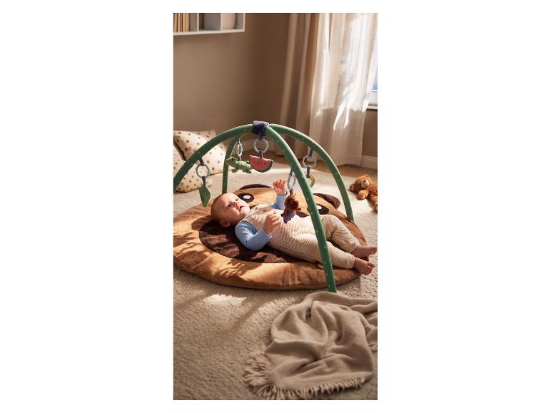 Baby spielt auf einer Spielmatte mit Spielbogen und hängendem Spielzeug.