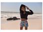 Frau in Sportkleidung am Strand: Jacke, Top und bedruckte Shorts.