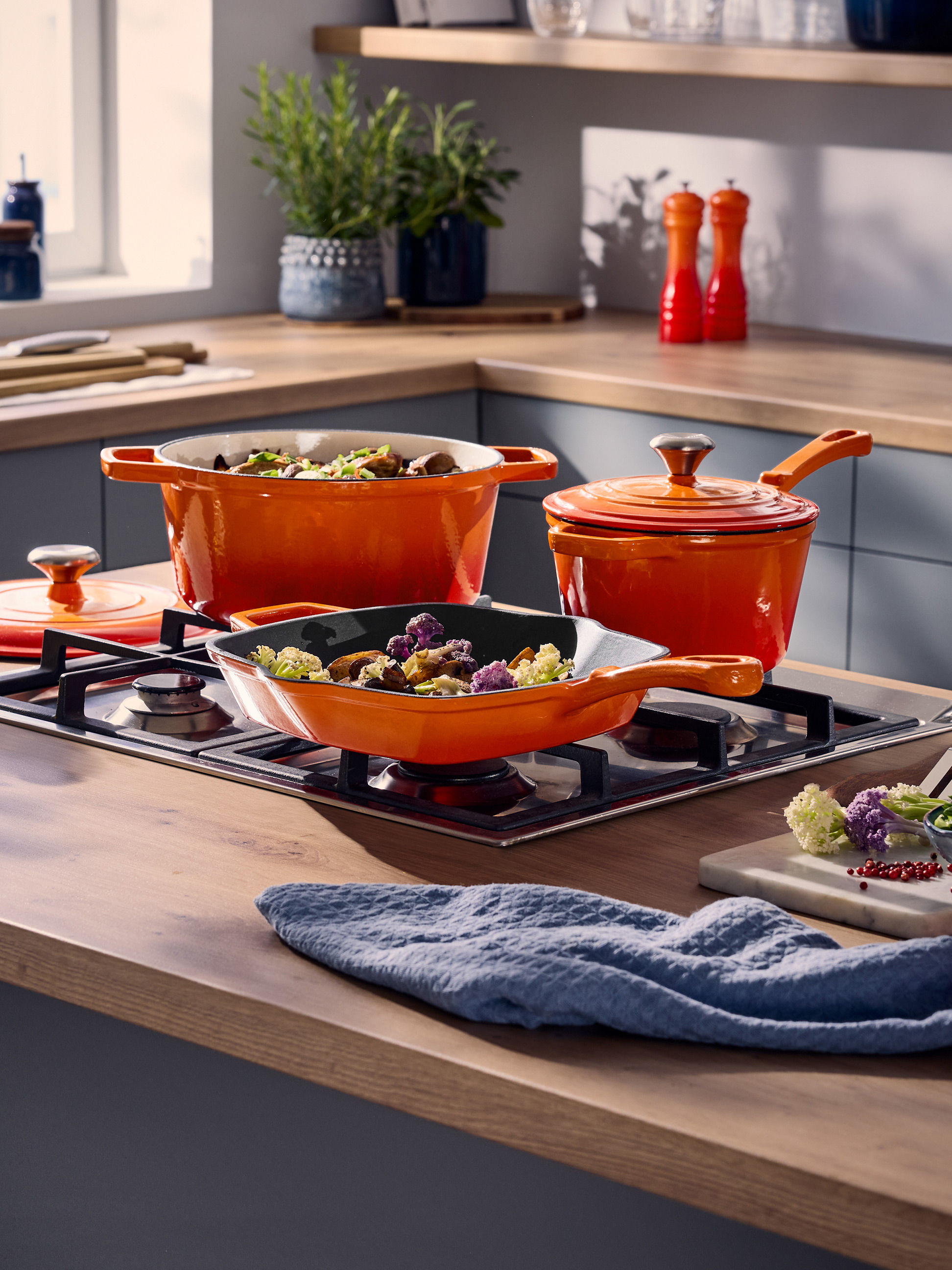 Orange Töpfe und Pfannen auf einem Gasherd in einer modernen Küche.