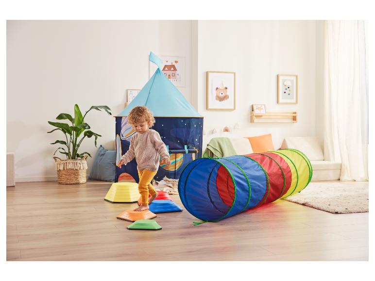 Kleinkind spielt auf bunten Trittsteinen und einem Spieltunnel in einem Kinderzimmer mit Zelt.