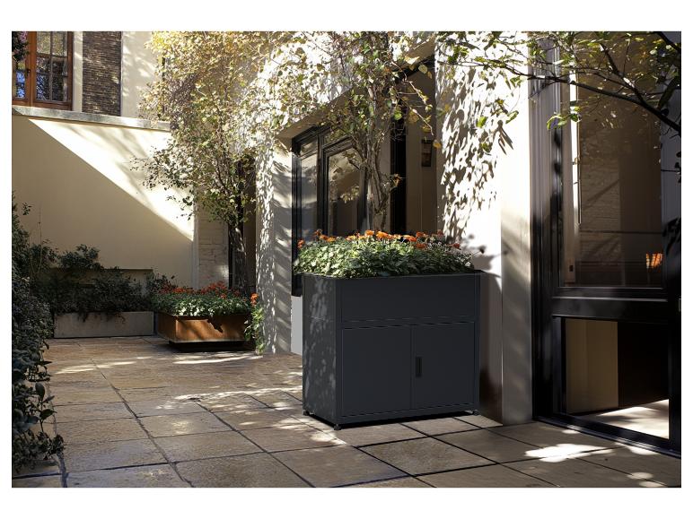 Pflanzkübel mit Aufbewahrungsschrank auf einer Terrasse mit Pflanzen und Platten.