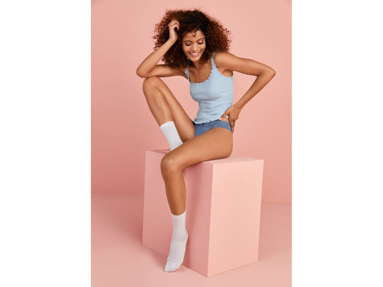 Eine Frau trägt ein blaues Tanktop, weiße Socken und blaue Unterwäsche.