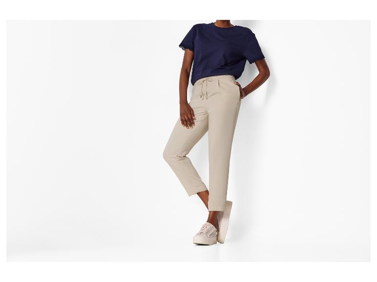 Frau in marineblauem T-Shirt mit Spitze und beiger Hose mit Kordelzug, dazu beige Sneaker.