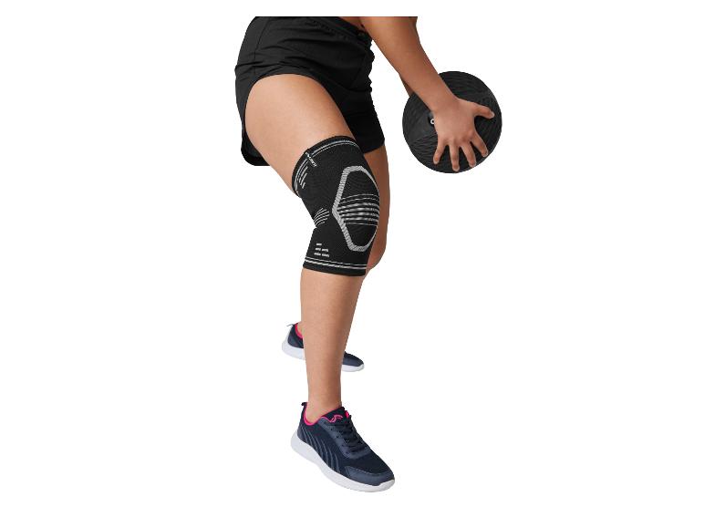 Person in schwarzen Sportshorts, Kniebandage und Turnschuhen, die einen Medizinball hält.
