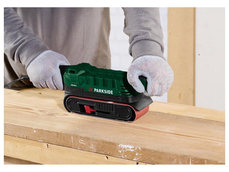 Person in Handschuhen schleift Holz mit einem grünen Parkside Bandschleifer.