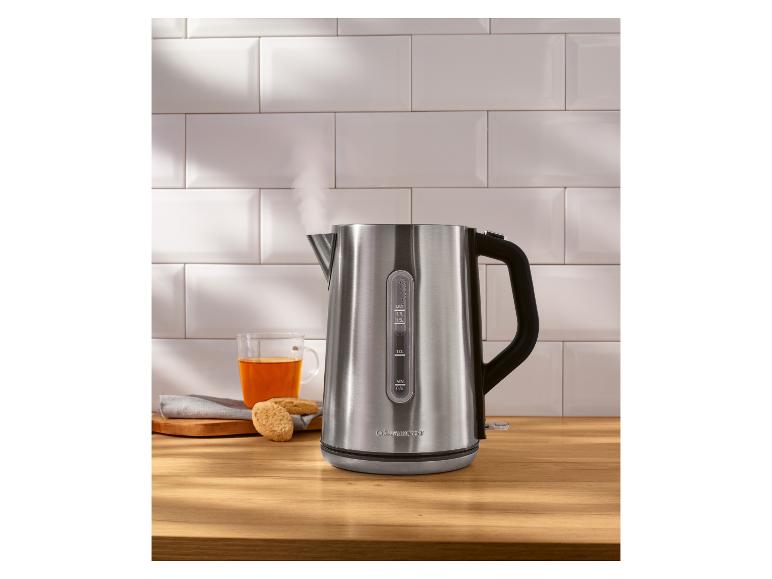 Edelstahlwasserkocher mit Dampf, neben einer Tasse Tee und Keksen.