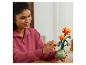 Lächelnde Frau arrangiert eine orangefarbene LEGO-Blume in einer grünen Vase.
