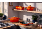 Oranges Gusseisen-Kochgeschirr auf einer hölzernen Küchenarbeitsplatte und einem Regal