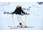 Skifahrerin in schwarzer Daunenjacke und weißer Skihose auf einer verschneiten Piste.