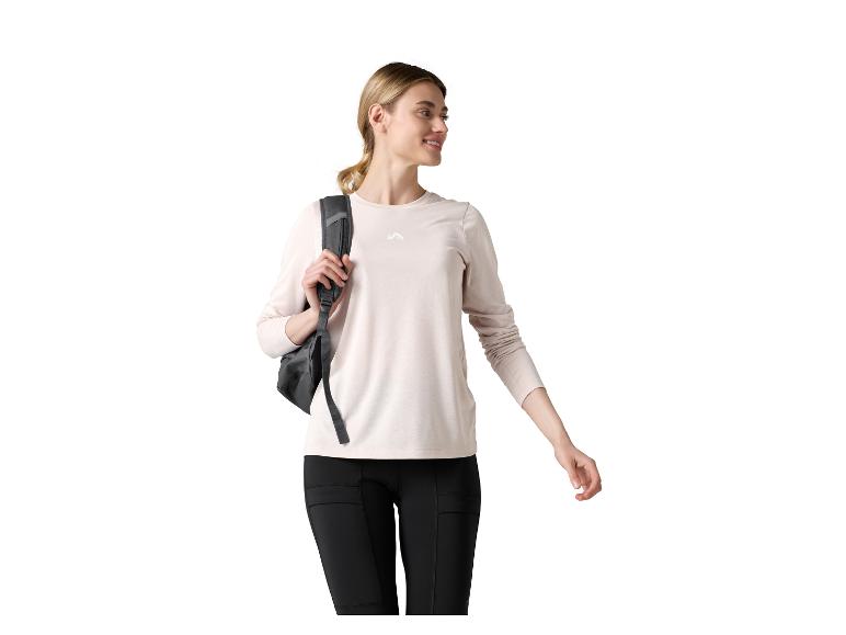 Lächelnde Frau mit grauem Rucksack, beigem Langarmshirt und schwarzen Leggings.