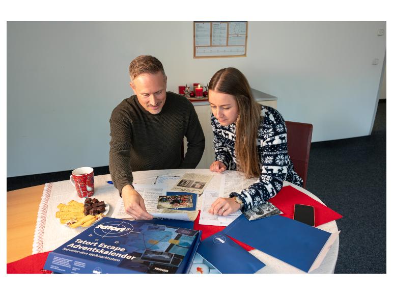Zwei Personen lösen einen Tatort Escape Adventskalender an einem Tisch.