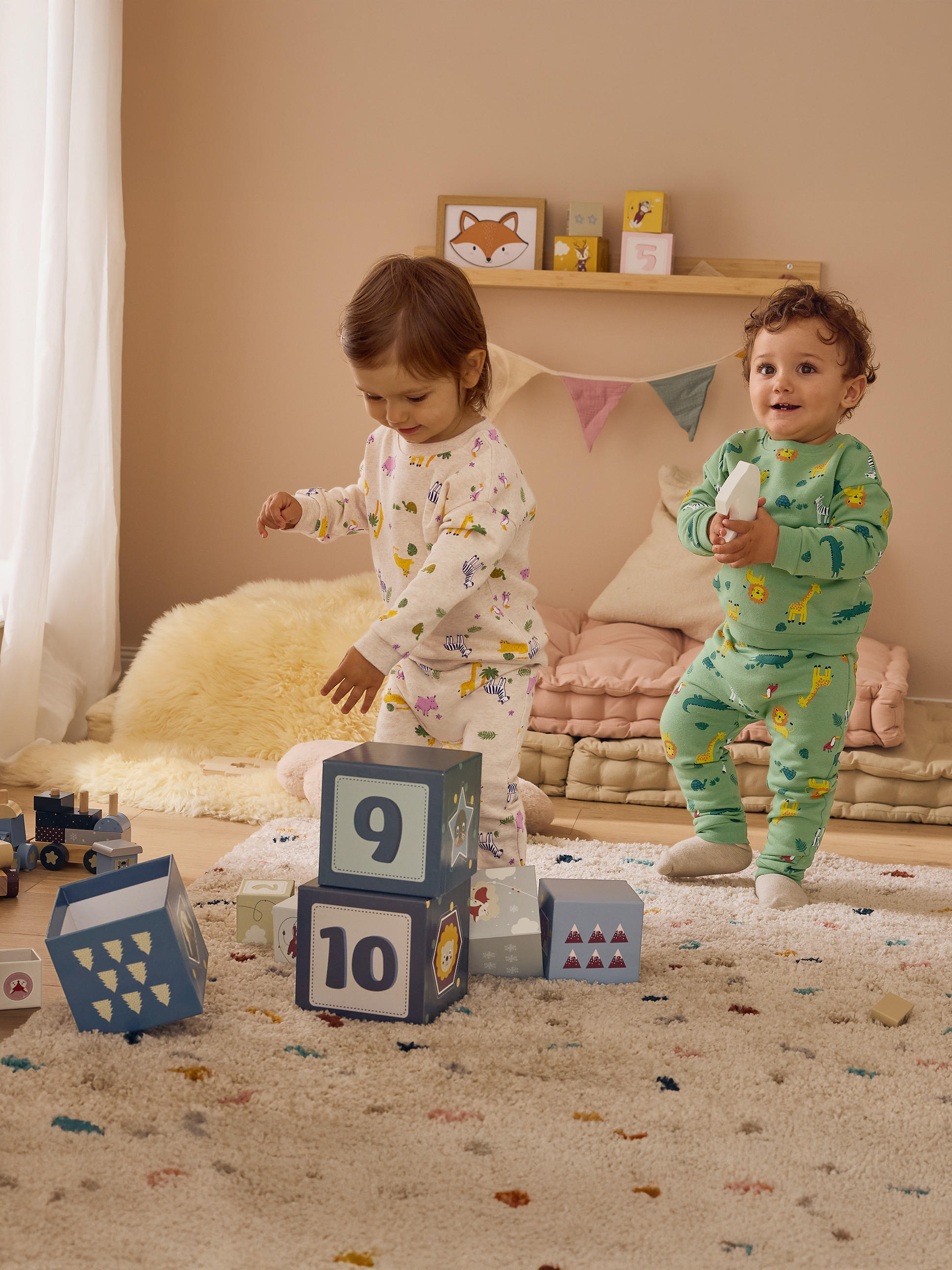 Zwei Kinder in Tier-Pyjamas spielen mit Bauklötzen in einem Zimmer.