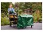 Eine Frau deckt Gartenmöbel mit einer grünen PARKSIDE Universal-Abdeckplane ab.