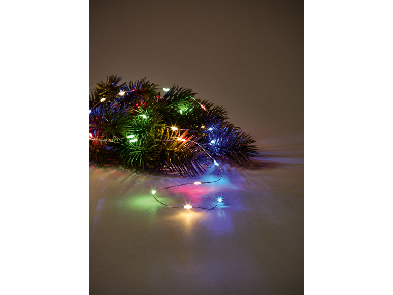 Tannenzweige mit bunten Weihnachtslichtern auf hellem Untergrund.
