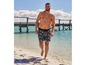 Mann in Badehose mit Palmenmuster am Strand.
