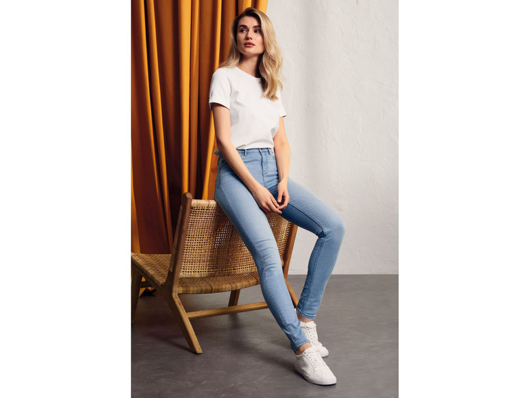 Eine Frau trägt ein weißes T-Shirt, blaue Skinny Jeans und weiße Sneaker.