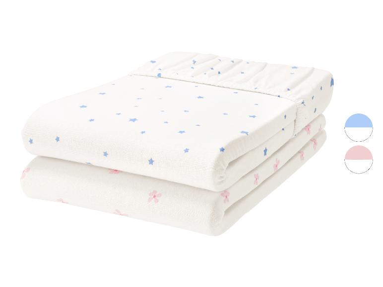 Set aus 2 Baby-Spannbettlaken, eines weiß mit blauen Sternen und eines weiß mit rosa Blumen.