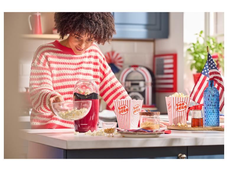 Frau füllt Popcorn aus einer roten Popcornmaschine in eine Schüssel, mit Popcornboxen und amerikanischen Flaggen.