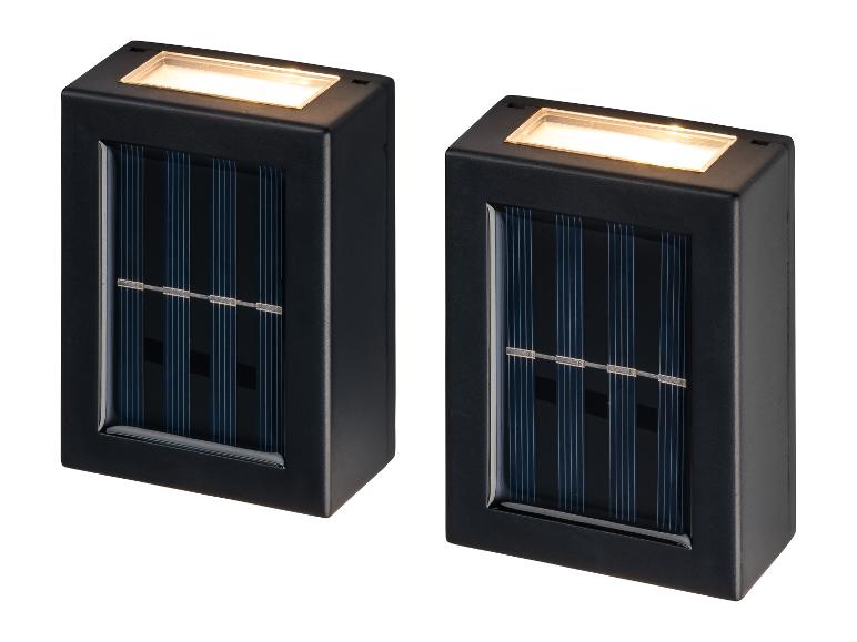 Zwei schwarze, rechteckige Solar-Wandleuchten mit integrierten Solarmodulen und warmweißem Licht.