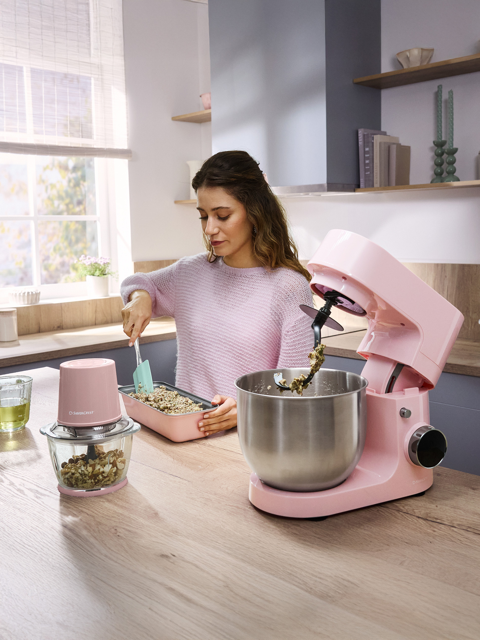 Frau bereitet Müsli mit einer rosa Küchenmaschine und einem Zerkleinerer zu.
