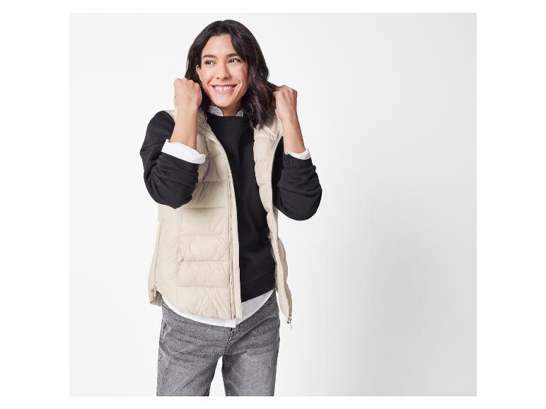 Lächelnde Frau mit beiger Weste und schwarzem Pullover.