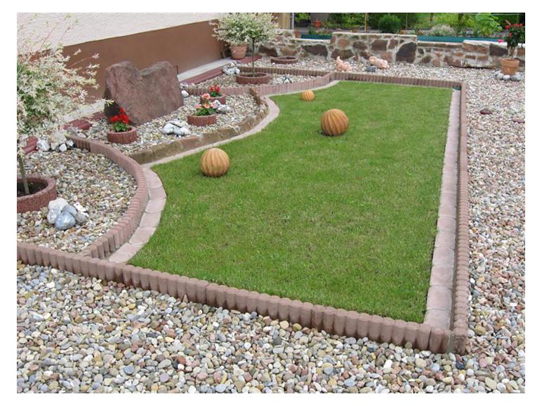 Garten mit Rasenfläche, Betonumrandungen und Kiesbeeten, dekoriert mit Pflanzen und Steinen.