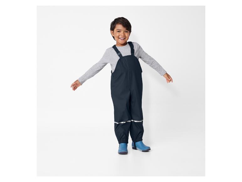 Ein Junge trägt blaue Gummistiefel und einen schwarzen Overall.