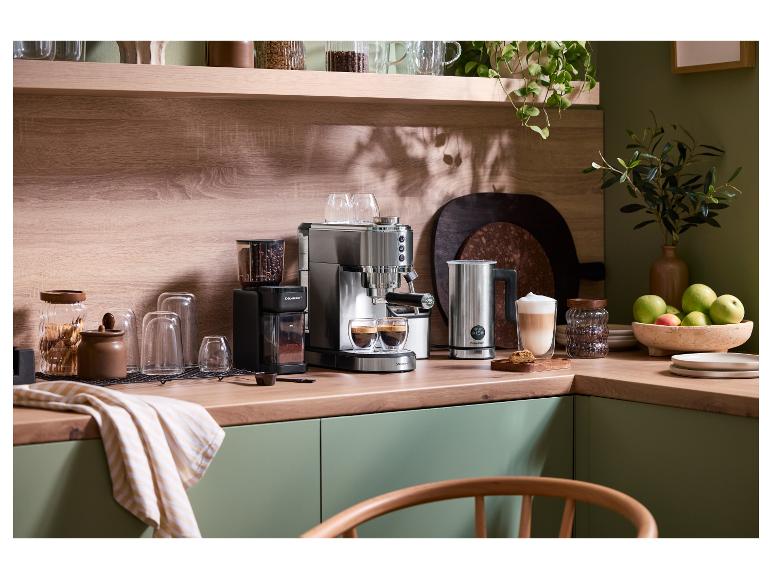 Kaffeemaschine und Mühle auf einer Holztheke mit grünen Schränken und Pflanzen.