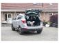 Silbernes Auto mit offenem Kofferraum und einem kleinen Hund neben einer Transportbox.