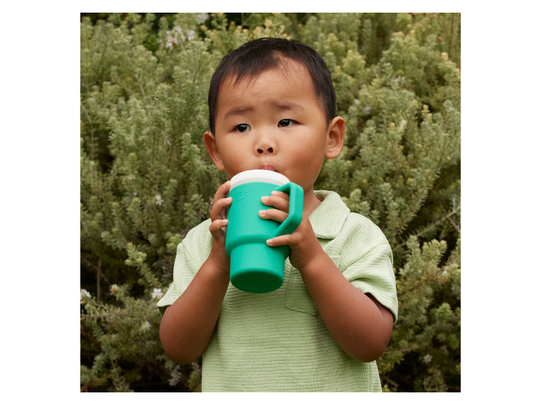 Ein Kleinkind trinkt aus einem grünen Becher mit Henkel.