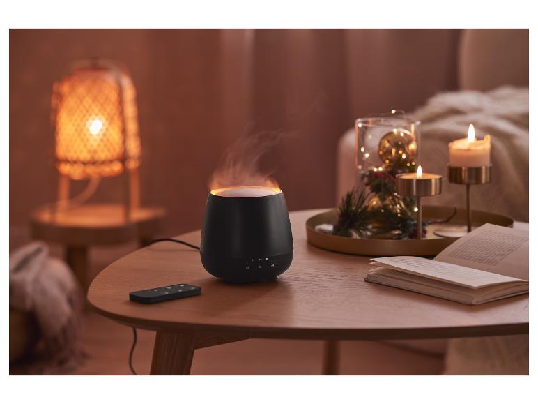 Ein schwarzer Aromadiffusor mit Fernbedienung auf einem Holztisch.