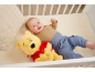 Lächelndes Baby liegt in einem Gitterbett neben einem gelben Plüschbären.