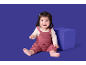 Glückliches Baby in einem rosa Strickstrampler sitzt neben einem blauen Würfel.