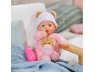 Weiche Babypuppe im rosa Strampler und Mütze mit Bärenohren neben einem Fläschchen.