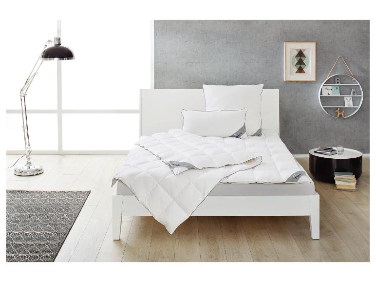 Weißes Bett mit Bettdecke und Kissen, Stehlampe, Teppich und Beistelltisch in einem modernen Schlafzimmer.