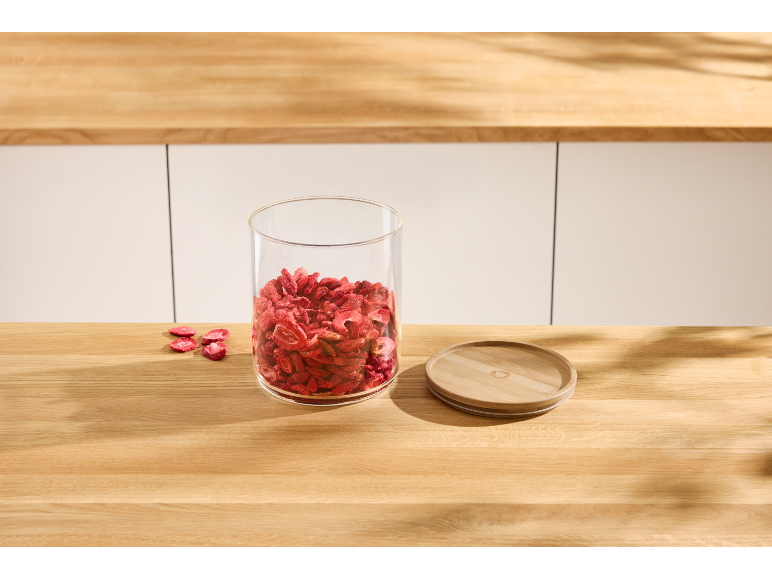 Vorratsglas mit getrockneten Erdbeeren und Holzdeckel auf einer Arbeitsplatte.