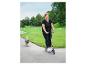 Lächelnde Frau auf einem rosa Roller mit einem Hund, der daneben in einem grünen Park läuft.