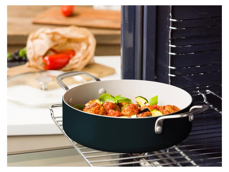 Ein Topf mit Fleischbällchen und Gemüse auf einem Ofenrost, mit frischen Zutaten im Hintergrund.