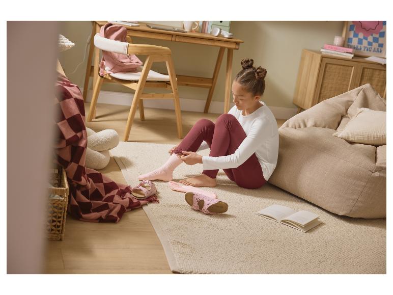 Mädchen zieht rosa Socken auf dem Boden an, mit Sandalen und einem Buch.