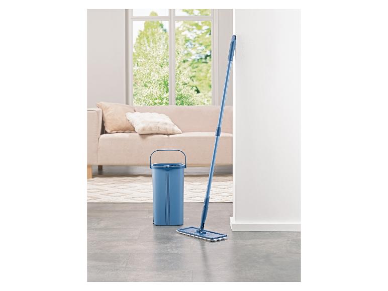 Blauer Eimer und Mopp in einem hellen Wohnzimmer mit Sofa und Fenster.