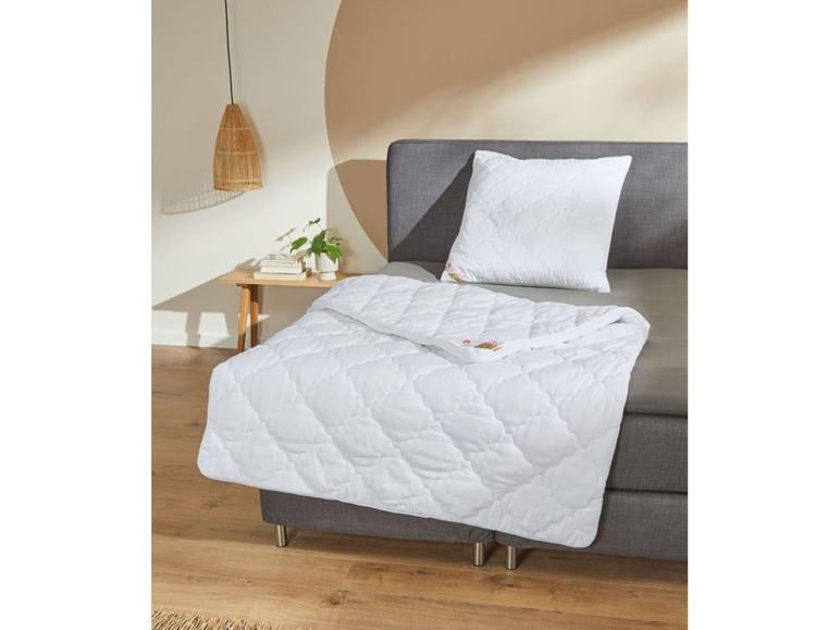 Eine weiße Bettdecke und ein Kissen auf einem grauen Bett.