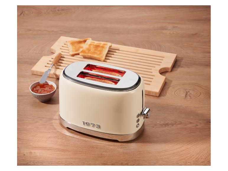 Cremefarbener Toaster mit Toast, Marmelade und Holzschneidebrett auf einem Holztisch.
