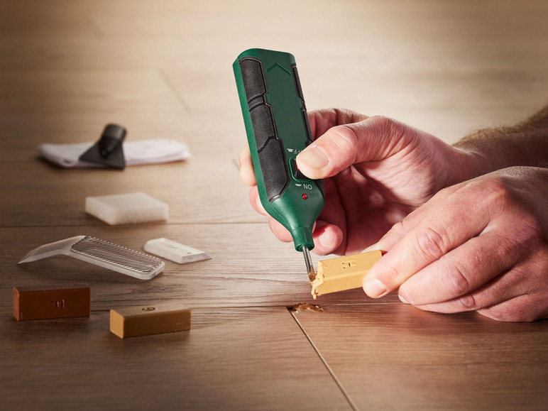 Eine Person repariert Holz mit einem Werkzeug und Holzspachtelmasse.