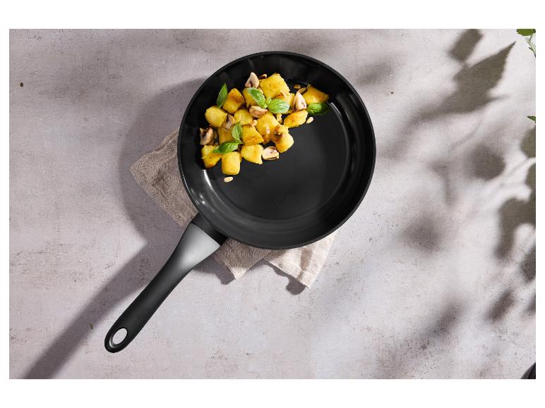 Bratpfanne mit gebratenen Kartoffeln, Pilzen und Basilikum auf hellem Hintergrund.