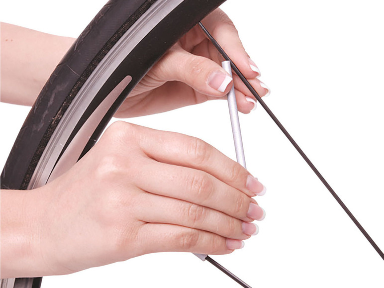 Nahaufnahme von Händen, die einen Fahrradreifen mit einem Werkzeug reparieren.