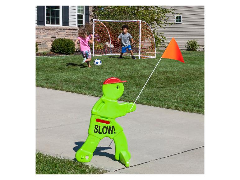 Kindersicherheitszeichen mit orangefarbener Flagge, Kinder spielen Fußball im Hintergrund.